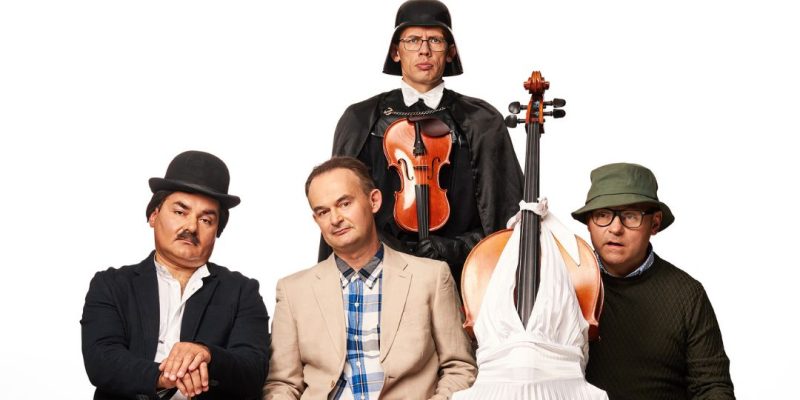 Czterech mężczyzn w humorystycznych kostiumach pozuje z instrumentami smyczkowymi na białym tle. Od lewej: mężczyzna w meloniku z laską, centralnie siedzący w beżowym garniturze ze skrzypcami na kolanach, za nim stojący w hełmie Dartha Vadera z czarną peleryną trzymający skrzypce, oraz mężczyzna w zielonej czapce bucket hat. Wiolonczela ubrana jest w białą suknię.