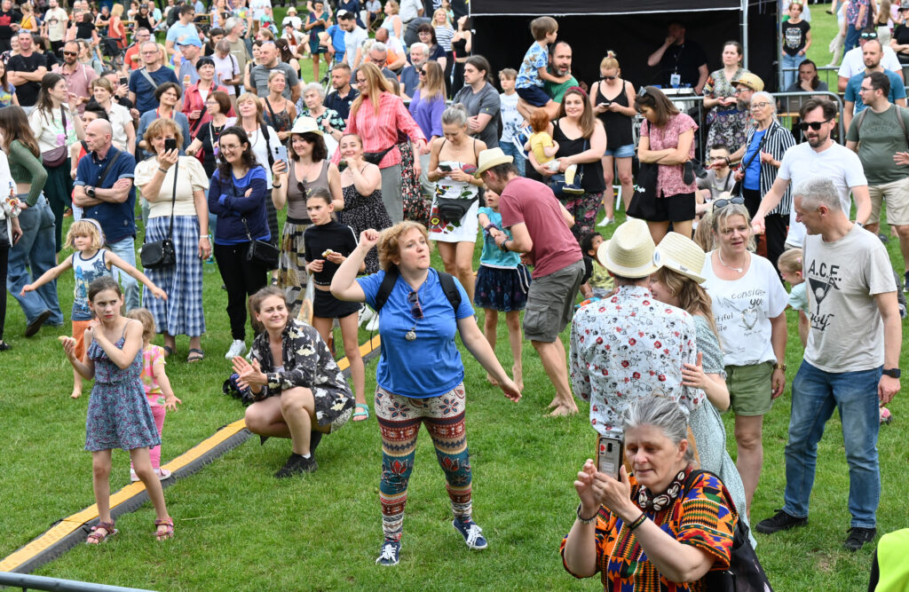 Zdjęcia z Festowalu KOrzenie Europy. Na zdjęciach widoczni są artyści na scenie, prowadzący koncert , publiczność i otoczenie koncertu - Park Bródnowski.