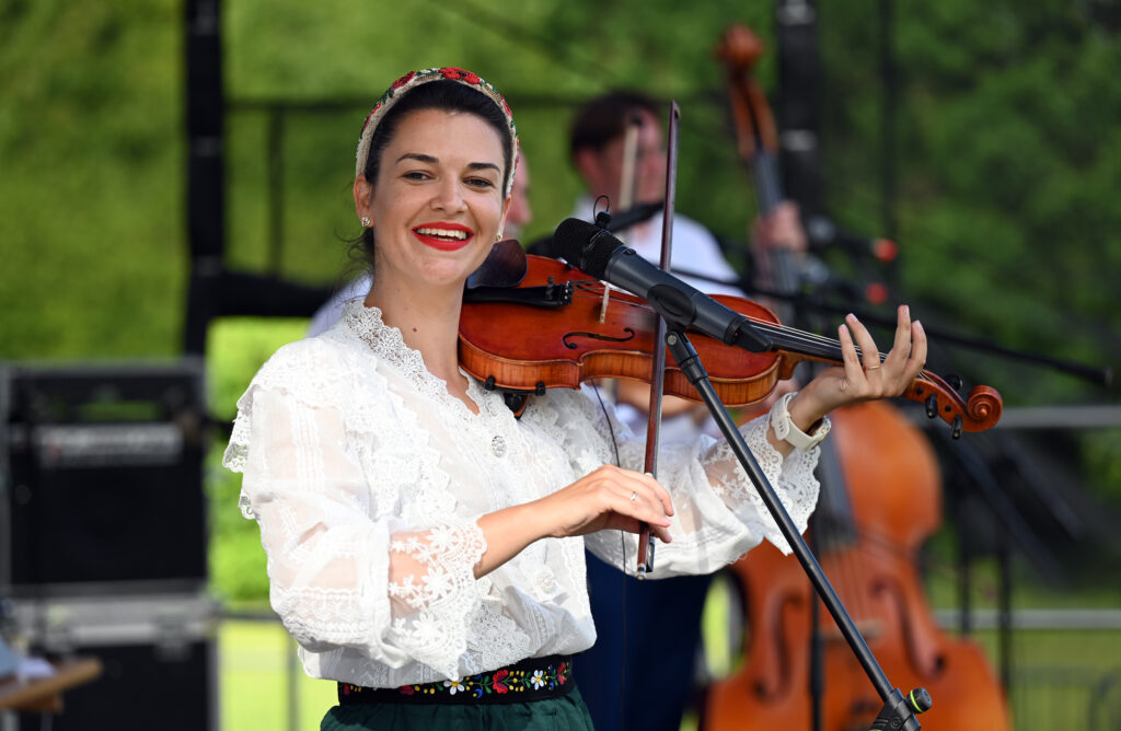 Zdjęcia z Festowalu KOrzenie Europy. Na zdjęciach widoczni są artyści na scenie, prowadzący koncert , publiczność i otoczenie koncertu - Park Bródnowski.