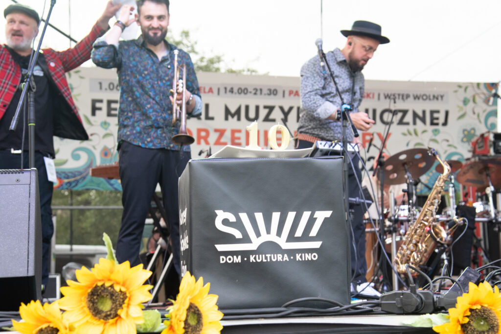 Zdjęcia z Festowalu KOrzenie Europy. Na zdjęciach widoczni są artyści na scenie, prowadzący koncert , publiczność i otoczenie koncertu - Park Bródnowski.