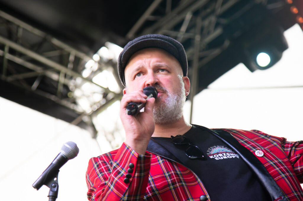 Zdjęcia z Festowalu KOrzenie Europy. Na zdjęciach widoczni są artyści na scenie, prowadzący koncert , publiczność i otoczenie koncertu - Park Bródnowski.