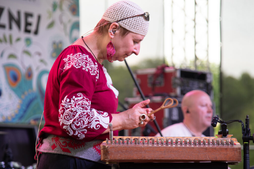 Zdjęcia z Festowalu KOrzenie Europy. Na zdjęciach widoczni są artyści na scenie, prowadzący koncert , publiczność i otoczenie koncertu - Park Bródnowski.