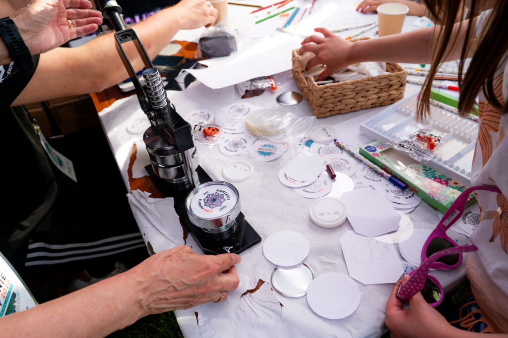 Zdjęcia z Festowalu KOrzenie Europy. Na zdjęciach widoczni są artyści na scenie, prowadzący koncert , publiczność i otoczenie koncertu - Park Bródnowski.