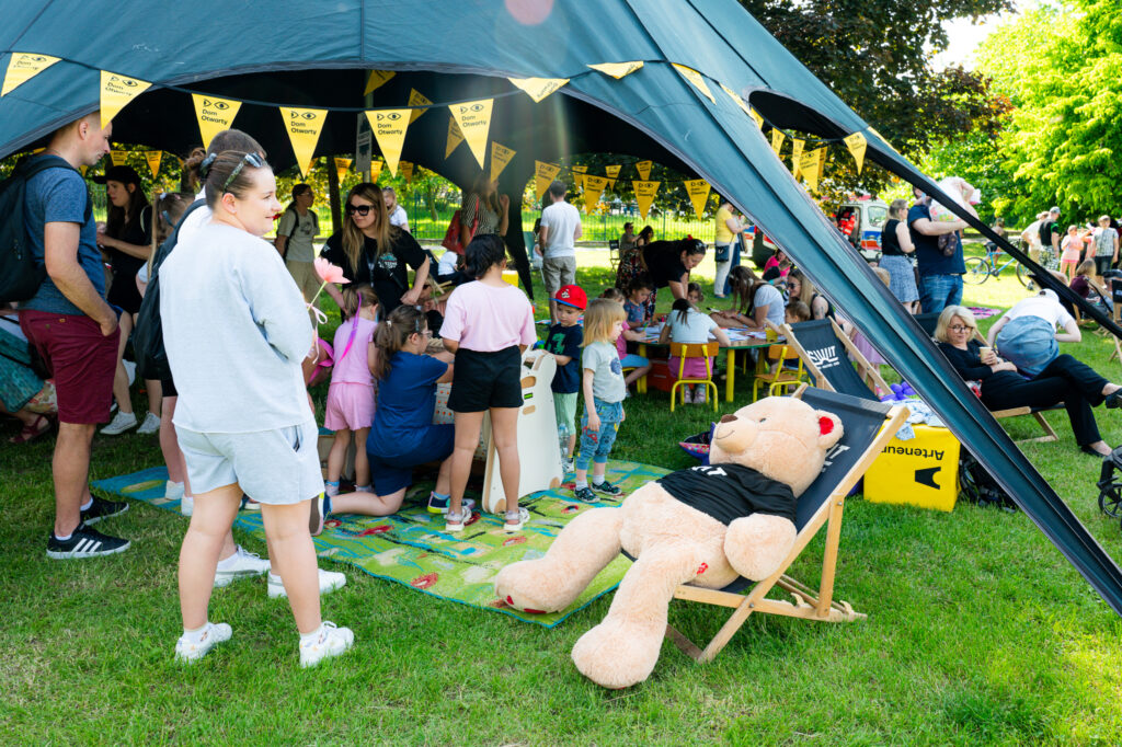 Zdjęcia z Festowalu KOrzenie Europy. Na zdjęciach widoczni są artyści na scenie, prowadzący koncert , publiczność i otoczenie koncertu - Park Bródnowski.