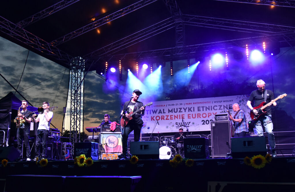 Zdjęcia z Festowalu KOrzenie Europy. Na zdjęciach widoczni są artyści na scenie, prowadzący koncert , publiczność i otoczenie koncertu - Park Bródnowski.