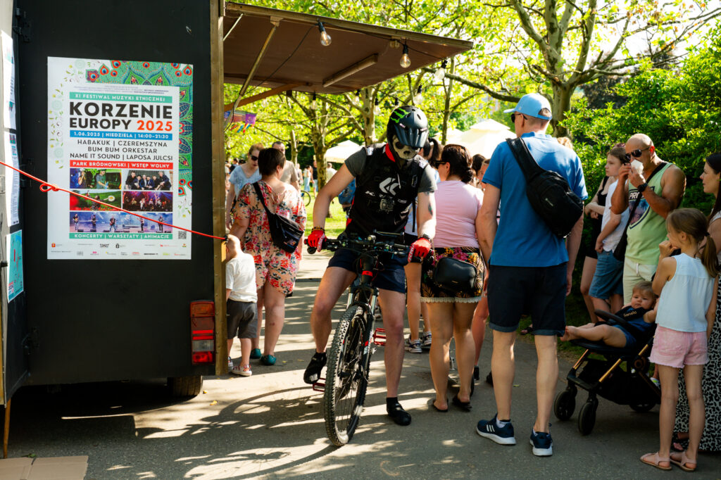 Zdjęcia z Festowalu KOrzenie Europy. Na zdjęciach widoczni są artyści na scenie, prowadzący koncert , publiczność i otoczenie koncertu - Park Bródnowski.