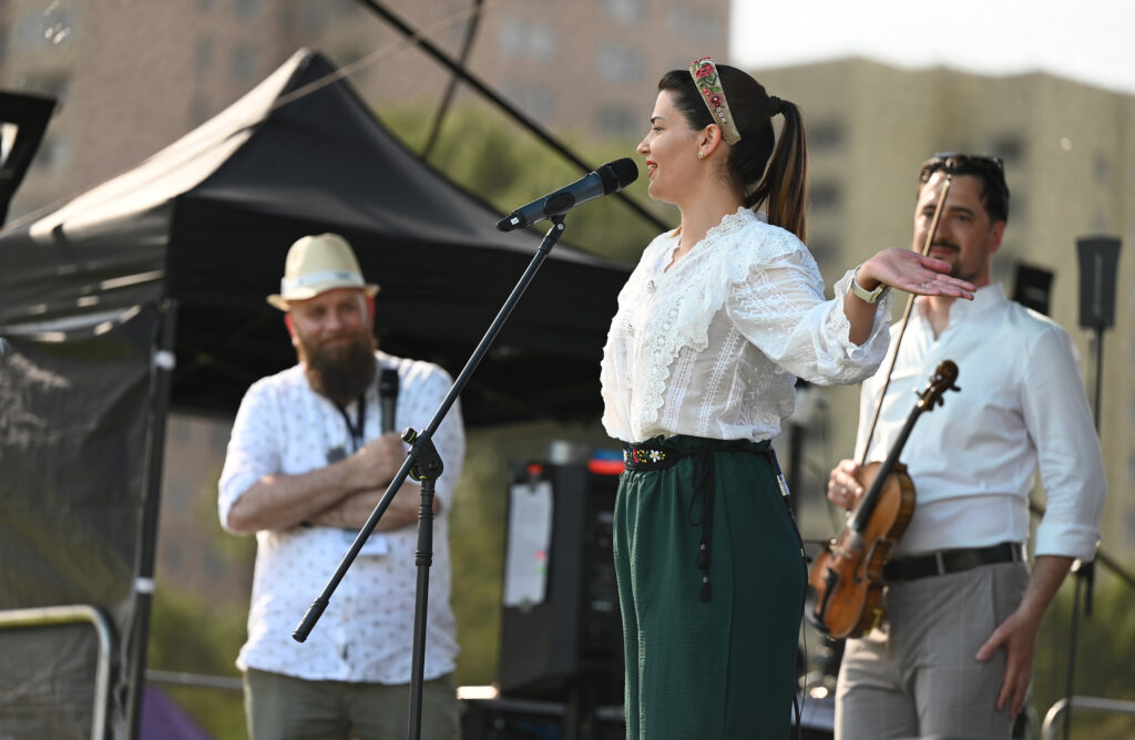 Zdjęcia z Festowalu KOrzenie Europy. Na zdjęciach widoczni są artyści na scenie, prowadzący koncert , publiczność i otoczenie koncertu - Park Bródnowski.