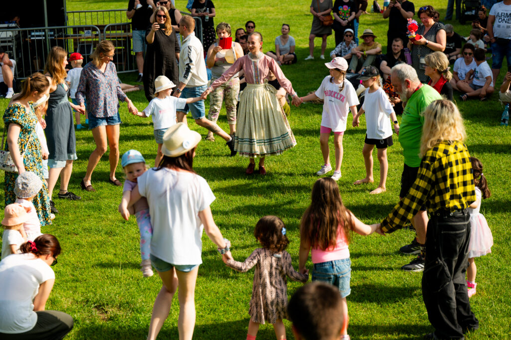 Zdjęcia z Festowalu KOrzenie Europy. Na zdjęciach widoczni są artyści na scenie, prowadzący koncert , publiczność i otoczenie koncertu - Park Bródnowski.