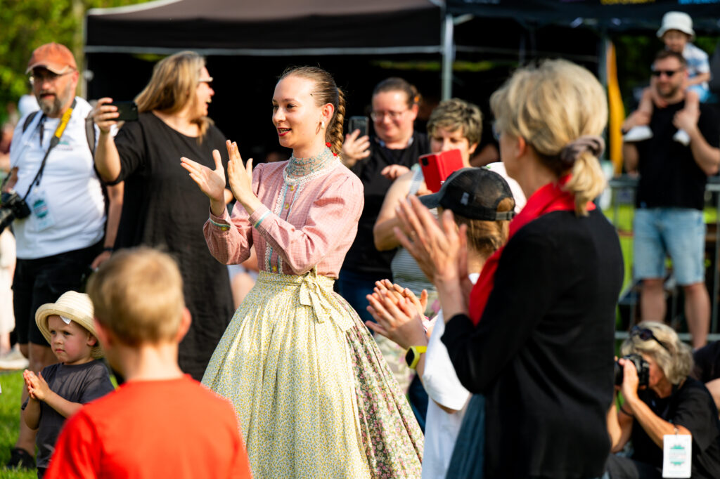 Zdjęcia z Festowalu KOrzenie Europy. Na zdjęciach widoczni są artyści na scenie, prowadzący koncert , publiczność i otoczenie koncertu - Park Bródnowski.
