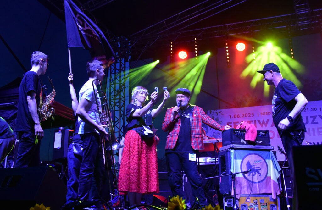 Zdjęcia z Festowalu KOrzenie Europy. Na zdjęciach widoczni są artyści na scenie, prowadzący koncert , publiczność i otoczenie koncertu - Park Bródnowski.