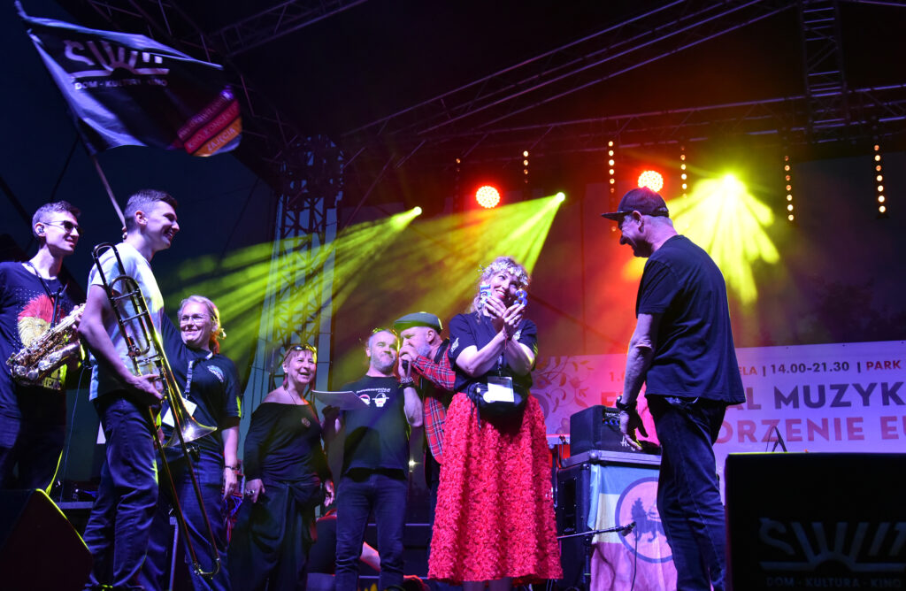 Zdjęcia z Festowalu KOrzenie Europy. Na zdjęciach widoczni są artyści na scenie, prowadzący koncert , publiczność i otoczenie koncertu - Park Bródnowski.