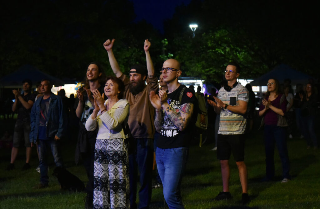 Zdjęcia z Festowalu KOrzenie Europy. Na zdjęciach widoczni są artyści na scenie, prowadzący koncert , publiczność i otoczenie koncertu - Park Bródnowski.