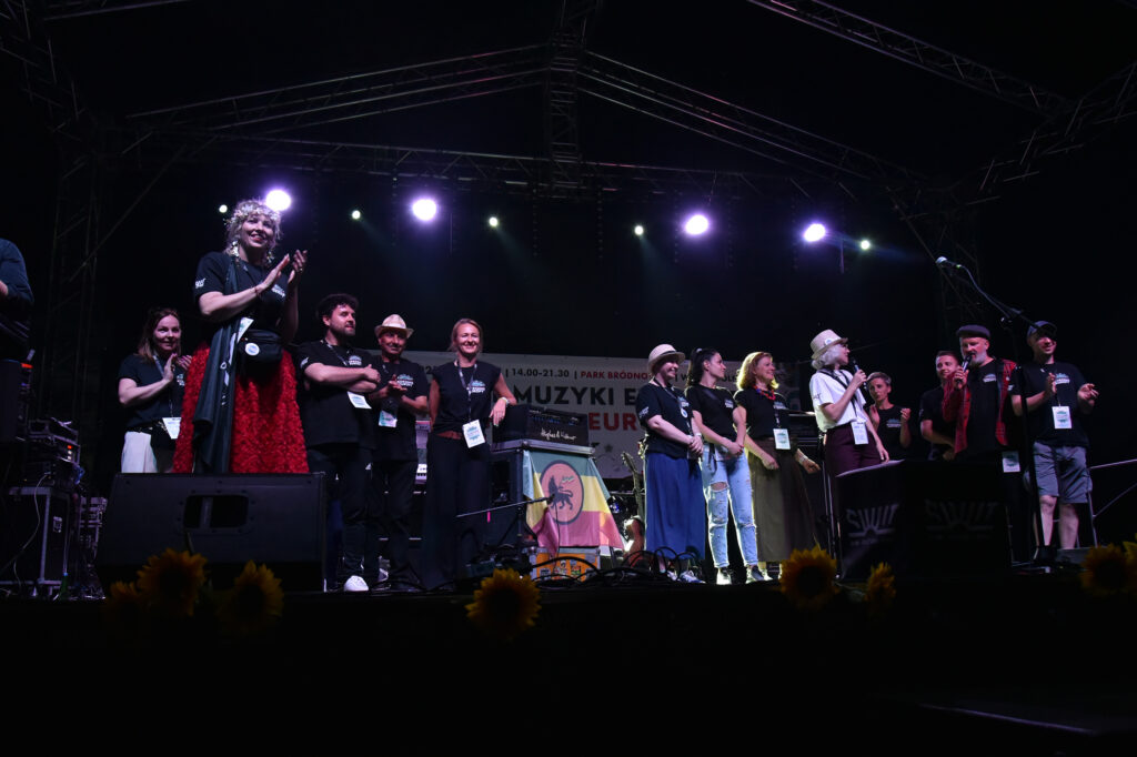 Zdjęcia z Festowalu KOrzenie Europy. Na zdjęciach widoczni są artyści na scenie, prowadzący koncert , publiczność i otoczenie koncertu - Park Bródnowski.