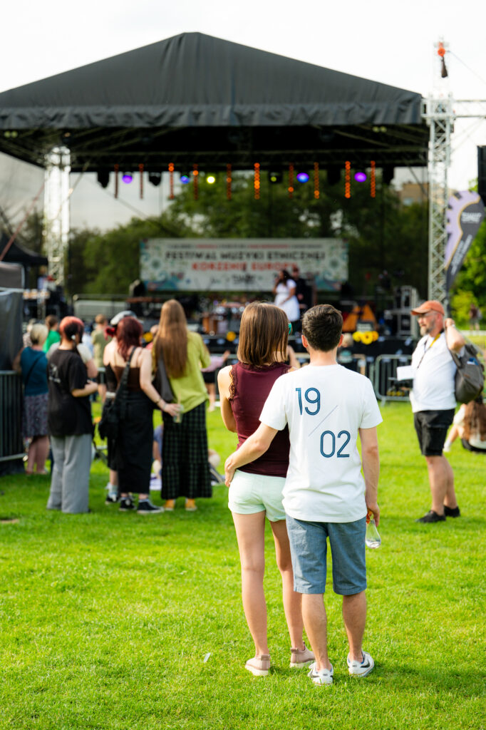 Zdjęcia z Festowalu KOrzenie Europy. Na zdjęciach widoczni są artyści na scenie, prowadzący koncert , publiczność i otoczenie koncertu - Park Bródnowski.