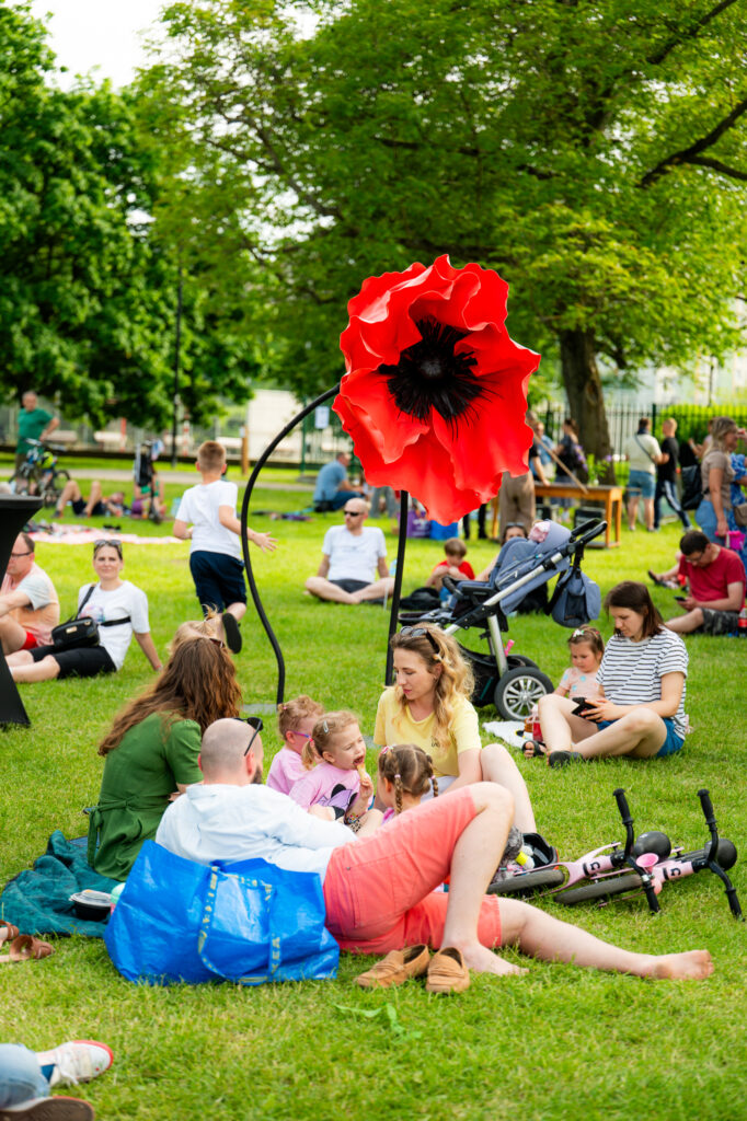 Zdjęcia z Festowalu KOrzenie Europy. Na zdjęciach widoczni są artyści na scenie, prowadzący koncert , publiczność i otoczenie koncertu - Park Bródnowski.