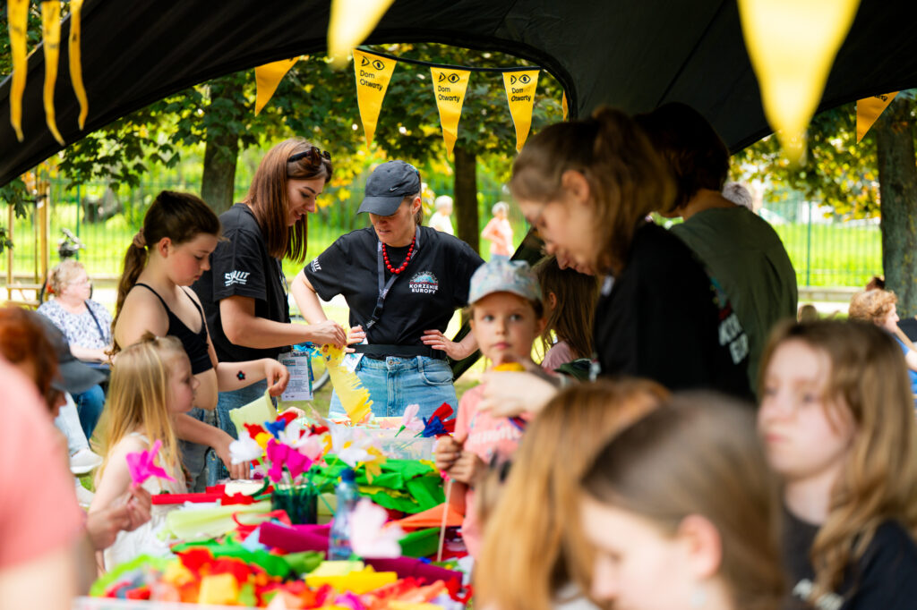 Zdjęcia z Festowalu KOrzenie Europy. Na zdjęciach widoczni są artyści na scenie, prowadzący koncert , publiczność i otoczenie koncertu - Park Bródnowski.