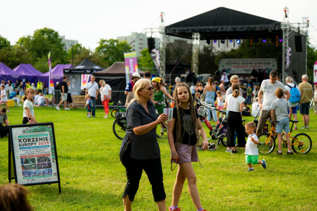 Zdjęcia z Festowalu KOrzenie Europy. Na zdjęciach widoczni są artyści na scenie, prowadzący koncert , publiczność i otoczenie koncertu - Park Bródnowski.