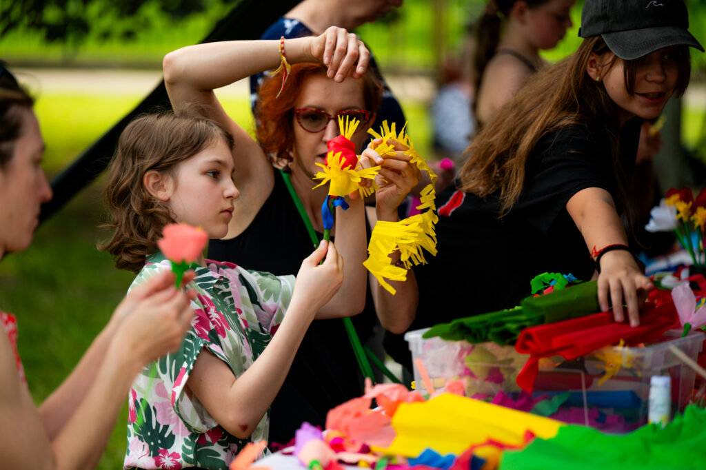 Zdjęcia z Festowalu KOrzenie Europy. Na zdjęciach widoczni są artyści na scenie, prowadzący koncert , publiczność i otoczenie koncertu - Park Bródnowski.