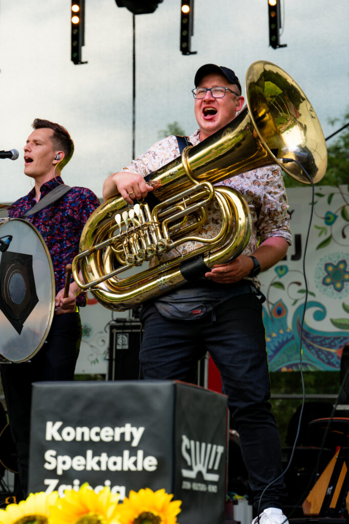 Zdjęcia z Festowalu KOrzenie Europy. Na zdjęciach widoczni są artyści na scenie, prowadzący koncert , publiczność i otoczenie koncertu - Park Bródnowski.