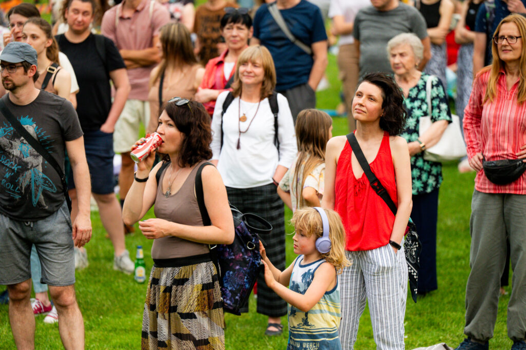 Zdjęcia z Festowalu KOrzenie Europy. Na zdjęciach widoczni są artyści na scenie, prowadzący koncert , publiczność i otoczenie koncertu - Park Bródnowski.
