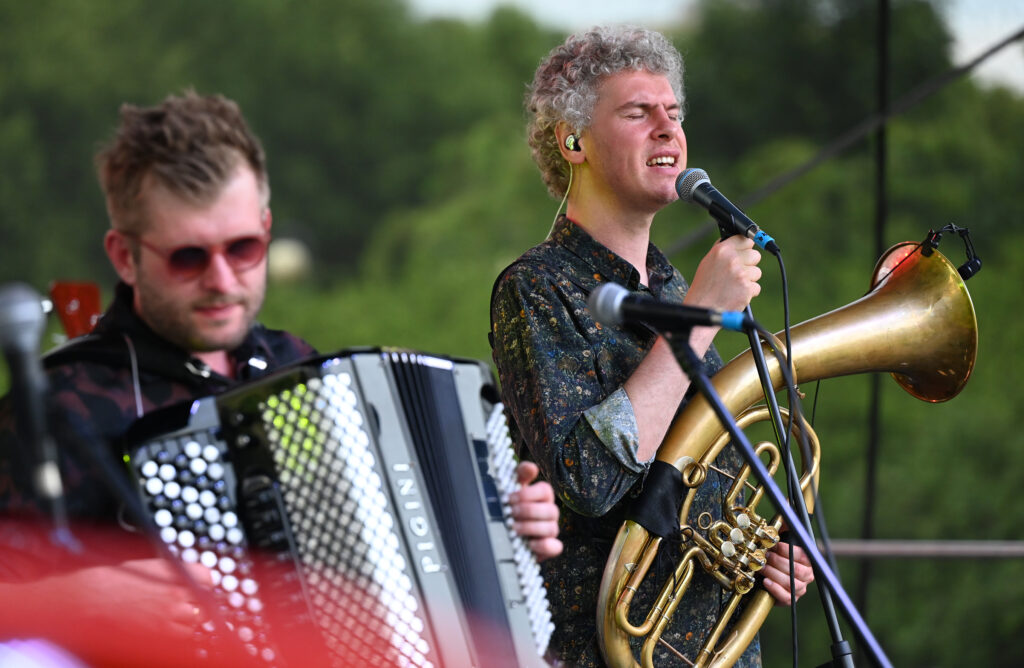 Zdjęcia z Festowalu KOrzenie Europy. Na zdjęciach widoczni są artyści na scenie, prowadzący koncert , publiczność i otoczenie koncertu - Park Bródnowski.