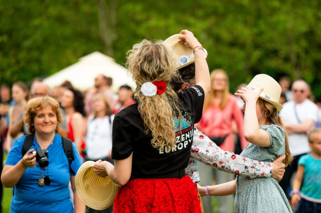 Zdjęcia z Festowalu KOrzenie Europy. Na zdjęciach widoczni są artyści na scenie, prowadzący koncert , publiczność i otoczenie koncertu - Park Bródnowski.