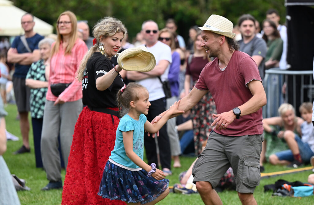 Zdjęcia z Festowalu KOrzenie Europy. Na zdjęciach widoczni są artyści na scenie, prowadzący koncert , publiczność i otoczenie koncertu - Park Bródnowski.