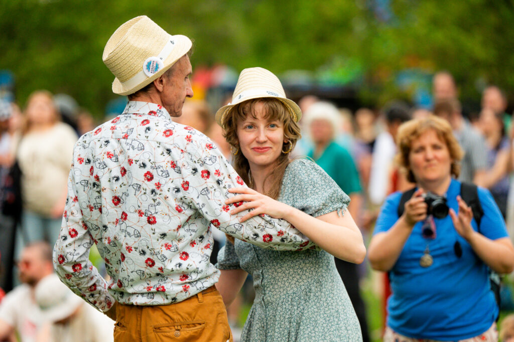 Zdjęcia z Festowalu KOrzenie Europy. Na zdjęciach widoczni są artyści na scenie, prowadzący koncert , publiczność i otoczenie koncertu - Park Bródnowski.