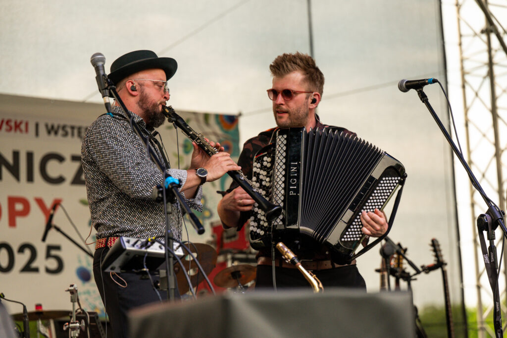 Zdjęcia z Festowalu KOrzenie Europy. Na zdjęciach widoczni są artyści na scenie, prowadzący koncert , publiczność i otoczenie koncertu - Park Bródnowski.