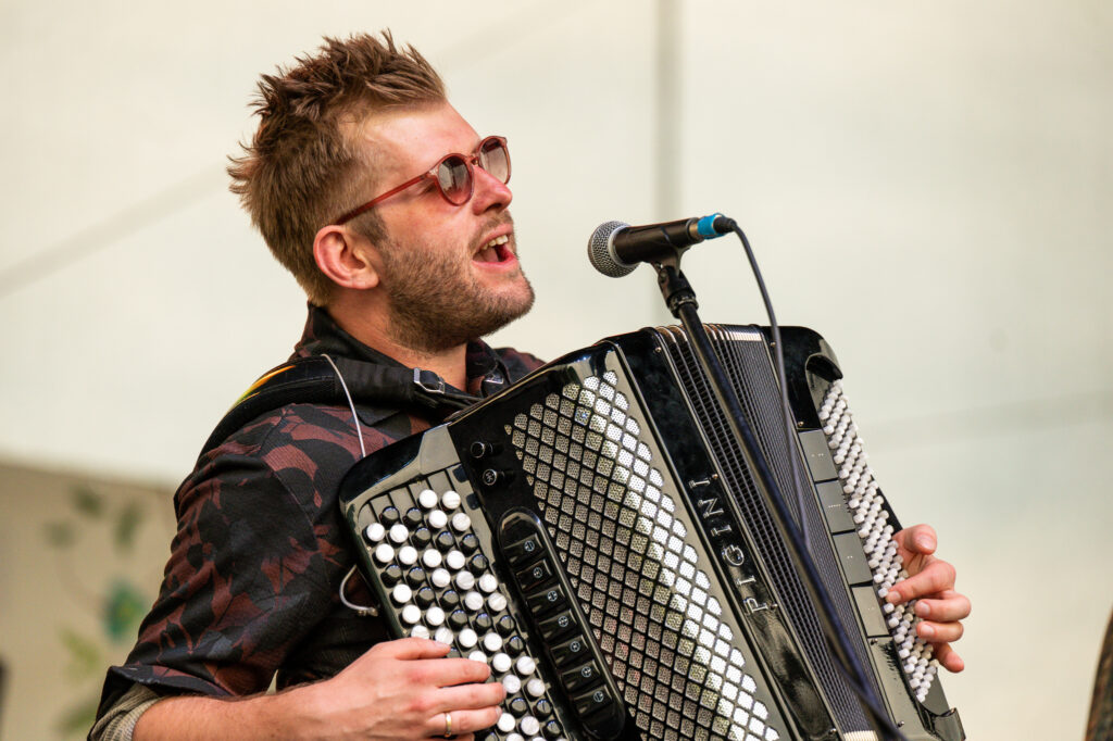 Zdjęcia z Festowalu KOrzenie Europy. Na zdjęciach widoczni są artyści na scenie, prowadzący koncert , publiczność i otoczenie koncertu - Park Bródnowski.