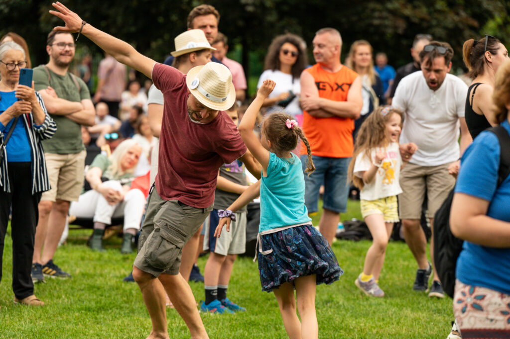 Zdjęcia z Festowalu KOrzenie Europy. Na zdjęciach widoczni są artyści na scenie, prowadzący koncert , publiczność i otoczenie koncertu - Park Bródnowski.