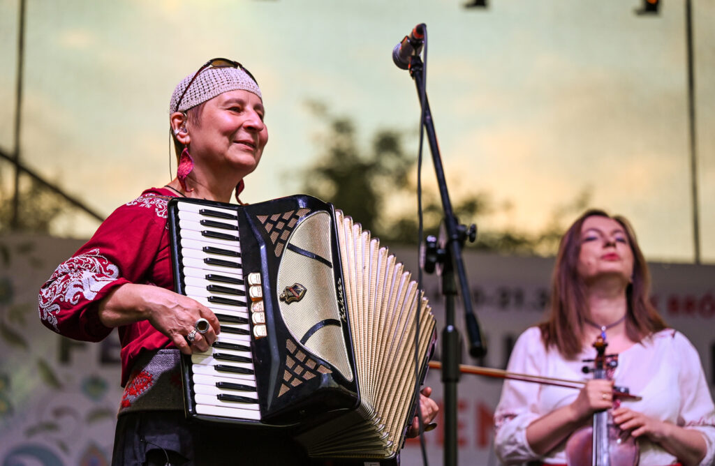 Zdjęcia z Festowalu KOrzenie Europy. Na zdjęciach widoczni są artyści na scenie, prowadzący koncert , publiczność i otoczenie koncertu - Park Bródnowski.