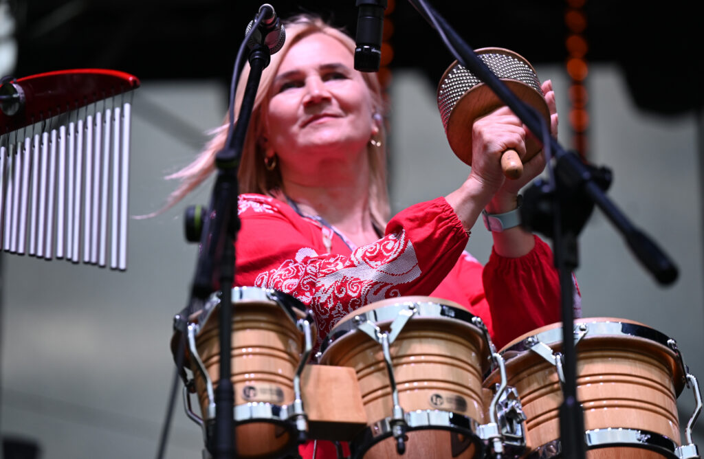 Zdjęcia z Festowalu KOrzenie Europy. Na zdjęciach widoczni są artyści na scenie, prowadzący koncert , publiczność i otoczenie koncertu - Park Bródnowski.