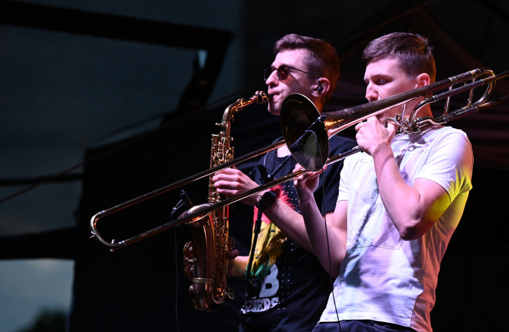 Zdjęcia z Festowalu KOrzenie Europy. Na zdjęciach widoczni są artyści na scenie, prowadzący koncert , publiczność i otoczenie koncertu - Park Bródnowski.