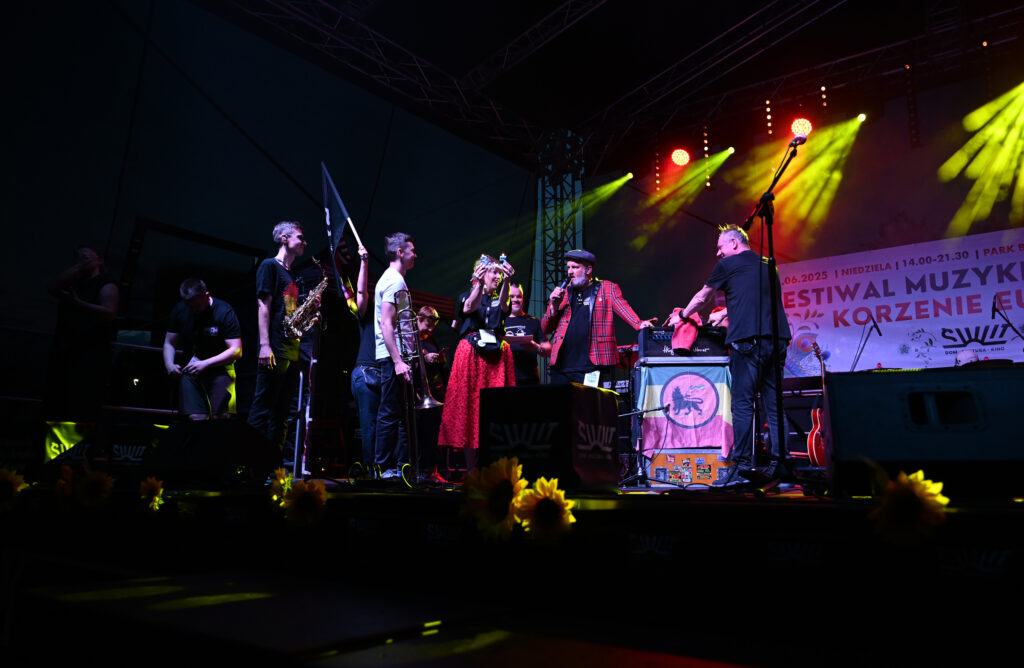 Zdjęcia z Festowalu KOrzenie Europy. Na zdjęciach widoczni są artyści na scenie, prowadzący koncert , publiczność i otoczenie koncertu - Park Bródnowski.