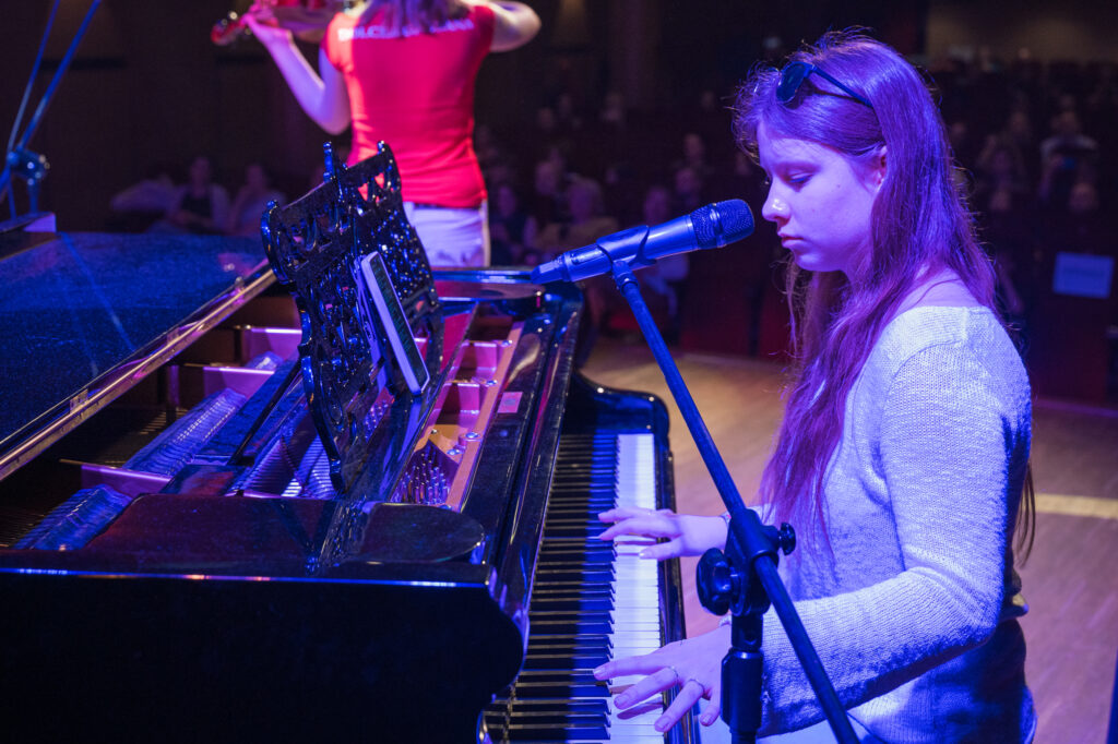 Zdjęcia z konkursu muzycznego dzieci i młodzieży Debiuty. Na o świetlonej scenie dziecięce zespołu i soliście, a przed sceną siedzi trzyosobowe jury.
