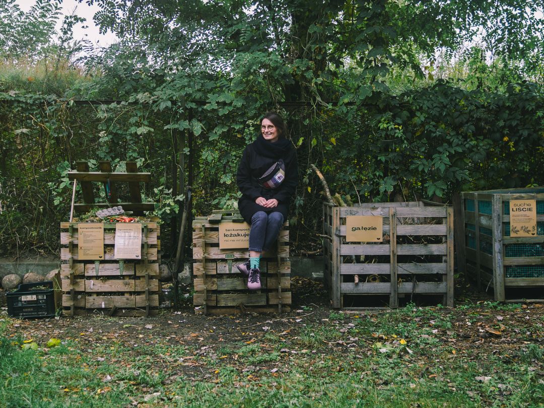 Kompostowniki w ogrodzie społecznym oznaczone tabliczkami.
