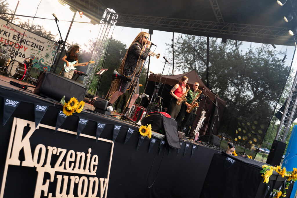Zdjęcia z XII Festiwalu Muzyki Etnicznej Korzenie Europy, który się odbył 31 maja 2026 r. w Parku Bródnowskich. Na zdjęciach scena plenerowa, zespoły muzyczne, organizatorzy i publiczność w otoczeniu zieleni parku.