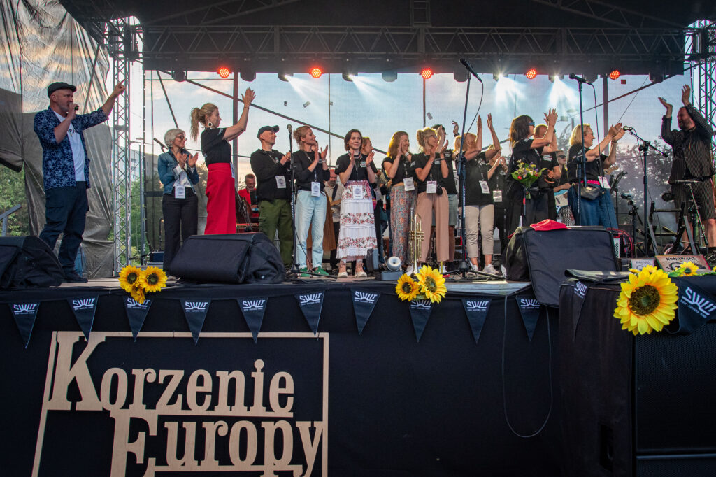 Zdjęcia z XII Festiwalu Muzyki Etnicznej Korzenie Europy, który się odbył 31 maja 2026 r. w Parku Bródnowskich. Na zdjęciach scena plenerowa, zespoły muzyczne, organizatorzy i publiczność w otoczeniu zieleni parku.