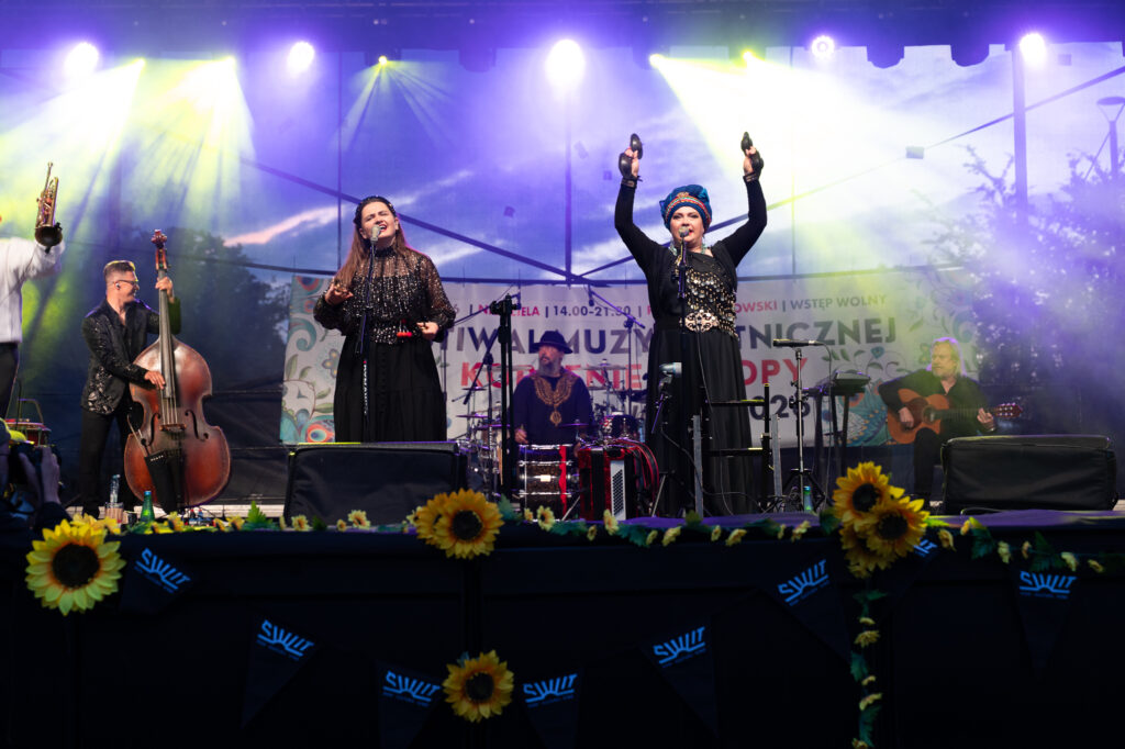 Zdjęcia z XII Festiwalu Muzyki Etnicznej Korzenie Europy, który się odbył 31 maja 2026 r. w Parku Bródnowskich. Na zdjęciach scena plenerowa, zespoły muzyczne, organizatorzy i publiczność w otoczeniu zieleni parku.