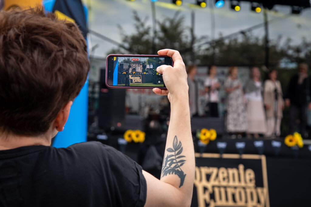 Zdjęcia z XII Festiwalu Muzyki Etnicznej Korzenie Europy, który się odbył 31 maja 2026 r. w Parku Bródnowskich. Na zdjęciach scena plenerowa, zespoły muzyczne, organizatorzy i publiczność w otoczeniu zieleni parku.