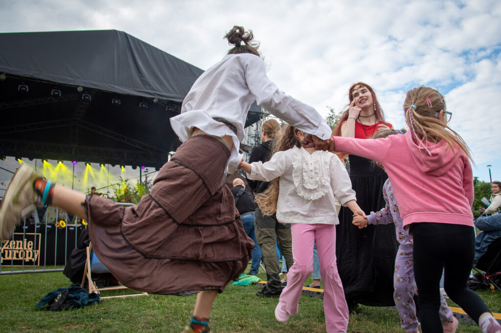 Zdjęcia z XII Festiwalu Muzyki Etnicznej Korzenie Europy, który się odbył 31 maja 2026 r. w Parku Bródnowskich. Na zdjęciach scena plenerowa, zespoły muzyczne, organizatorzy i publiczność w otoczeniu zieleni parku.