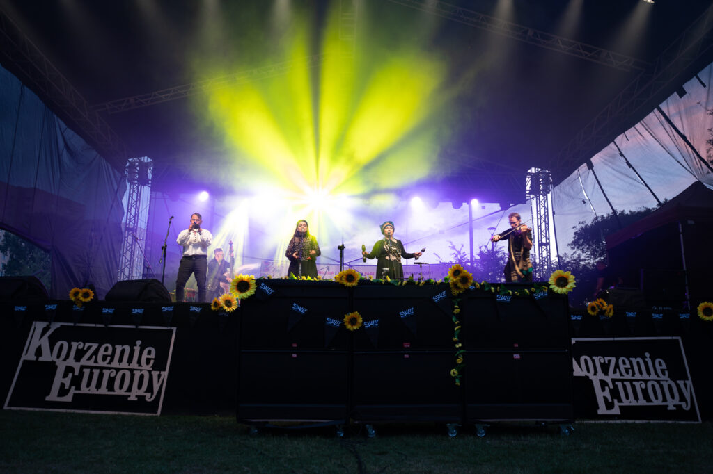 Zdjęcia z XII Festiwalu Muzyki Etnicznej Korzenie Europy, który się odbył 31 maja 2026 r. w Parku Bródnowskich. Na zdjęciach scena plenerowa, zespoły muzyczne, organizatorzy i publiczność w otoczeniu zieleni parku.