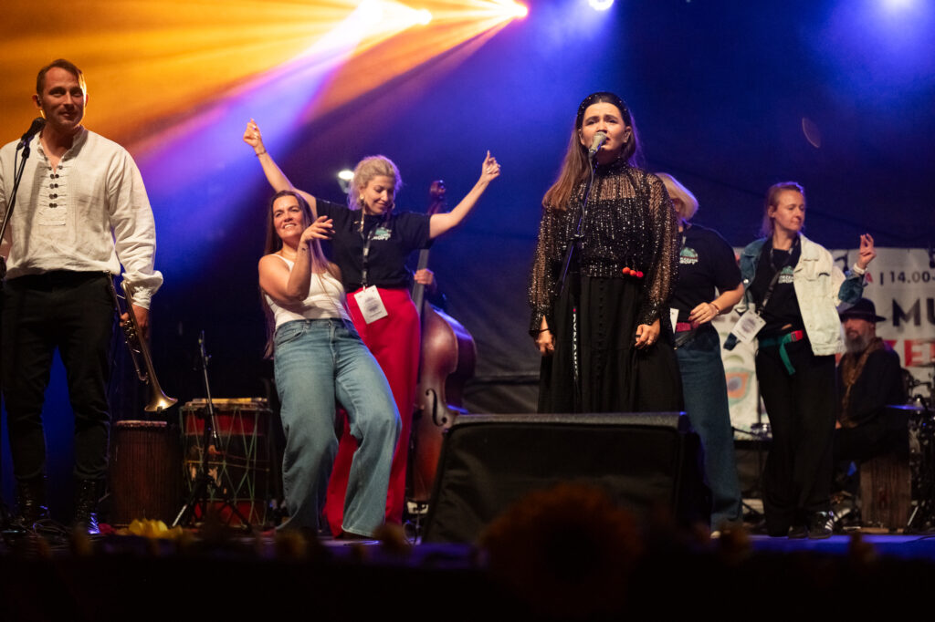 Zdjęcia z XII Festiwalu Muzyki Etnicznej Korzenie Europy, który się odbył 31 maja 2026 r. w Parku Bródnowskich. Na zdjęciach scena plenerowa, zespoły muzyczne, organizatorzy i publiczność w otoczeniu zieleni parku.