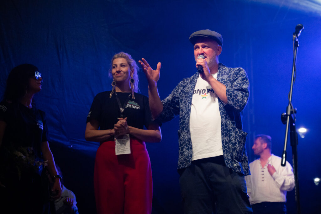 Zdjęcia z XII Festiwalu Muzyki Etnicznej Korzenie Europy, który się odbył 31 maja 2026 r. w Parku Bródnowskich. Na zdjęciach scena plenerowa, zespoły muzyczne, organizatorzy i publiczność w otoczeniu zieleni parku.
