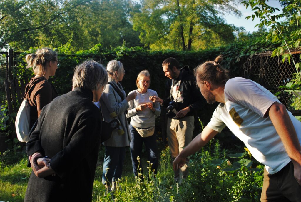 Grupa osób ogląda rośliny rosnące na pryzmie kompostowej.