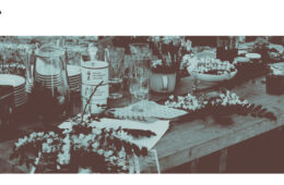 Stół na którym znajdują się szklanki, serwetki, talerze i kwitnąca robinia akacjowa.