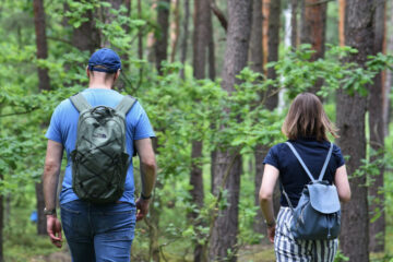Kobieta i mężczyzna, odwróceni tyłem, idą przez zielony las.