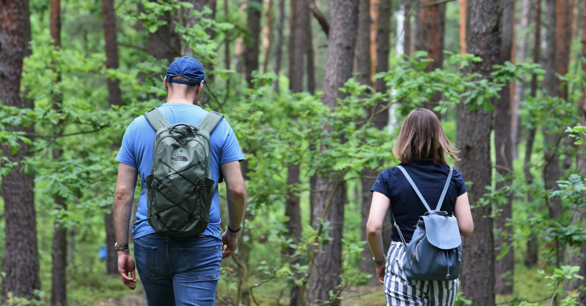 Kobieta i mężczyzna, odwróceni tyłem, idą przez zielony las.