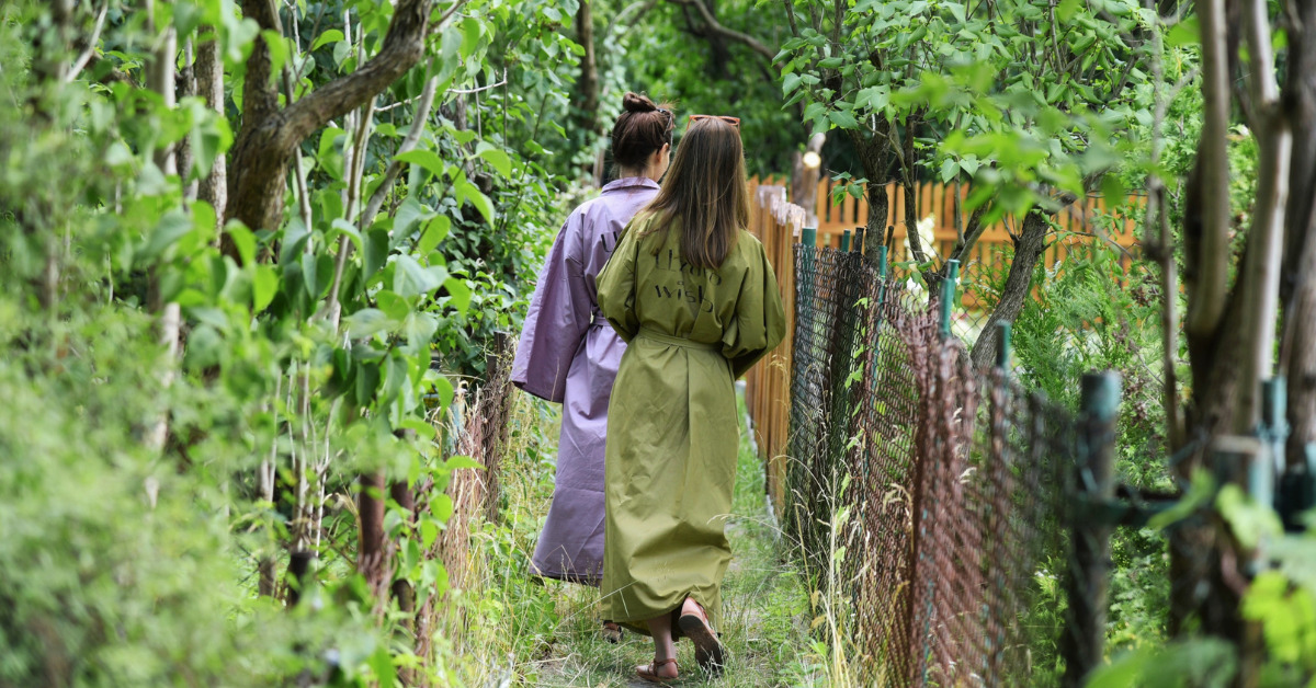 Dwie kobiety w szlafrokach z napisem Uzdrowisko idą przez ogrody działkowe.